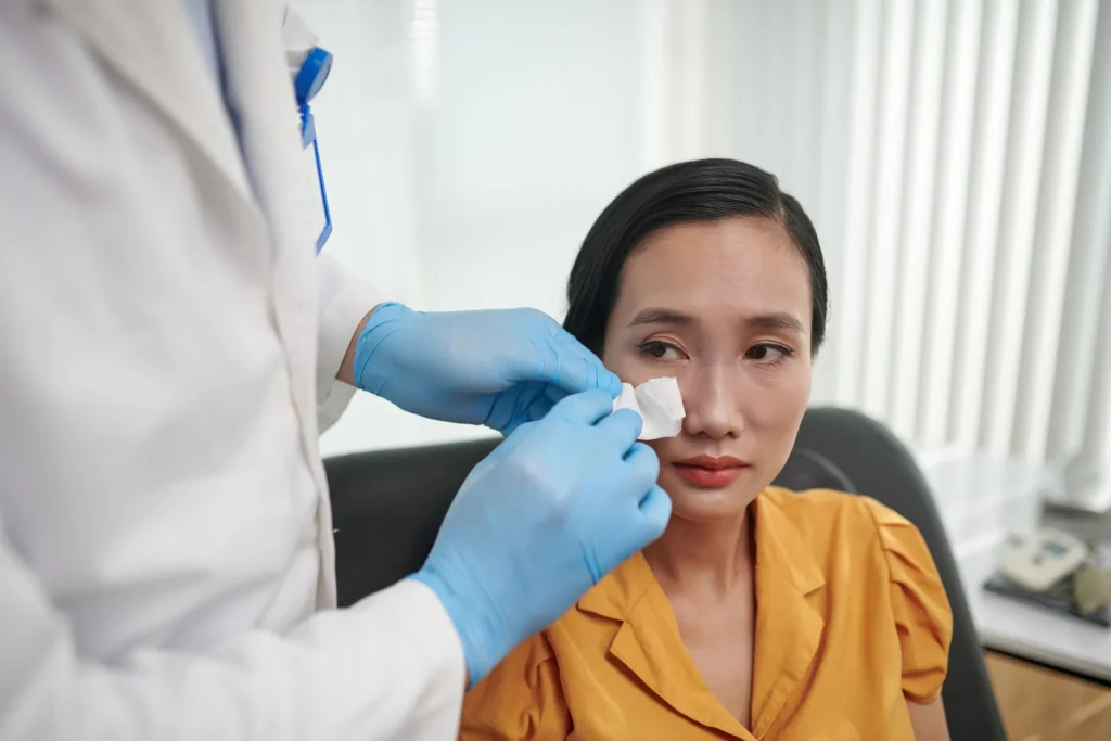 Doctor examining patient’s nose during rhinoplasty recovery follow-up appointment.