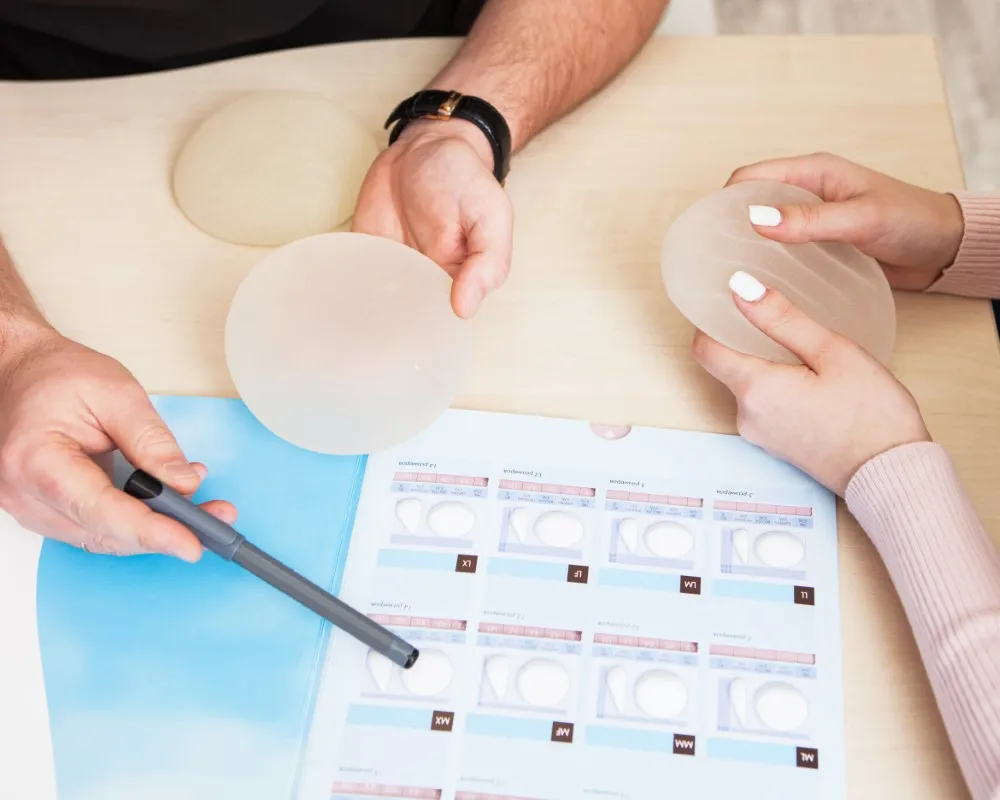 Close-up of silicone and saline breast implants displayed on a surgeon’s desk as part of a detailed patient consultation comparing breast lift vs breast augmentation options