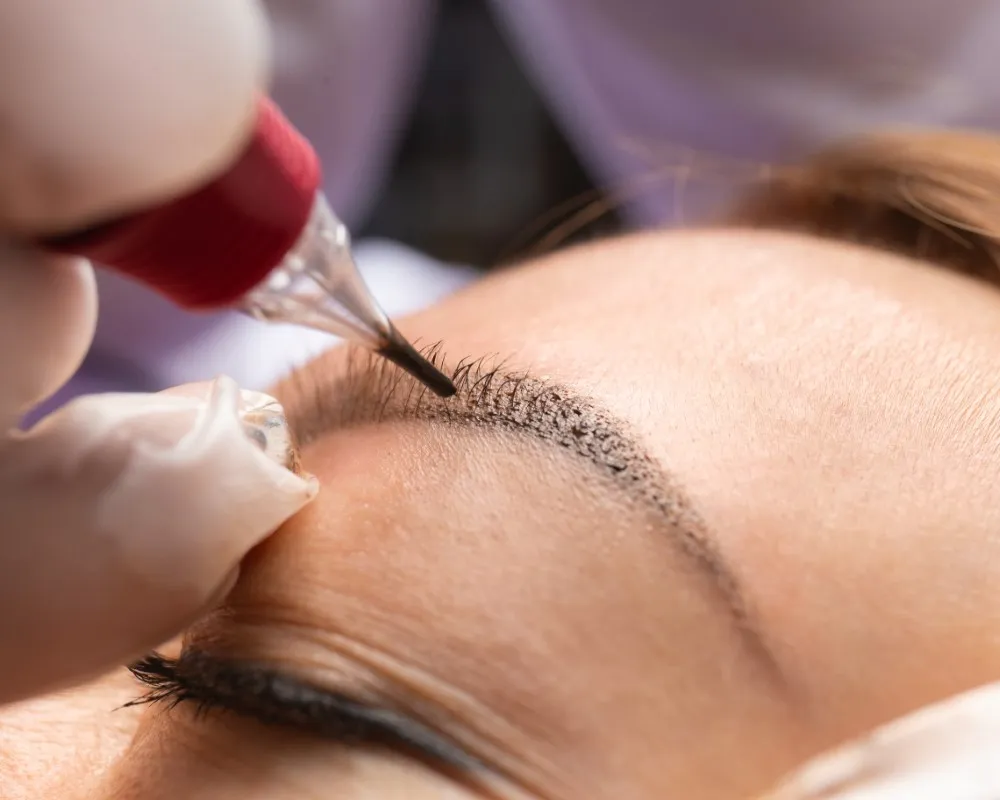 A woman receiving a microblading session for her eyebrows, with hair-like strokes being manually applied to enhance shape and volume in the context of microblading vs micropigmentation