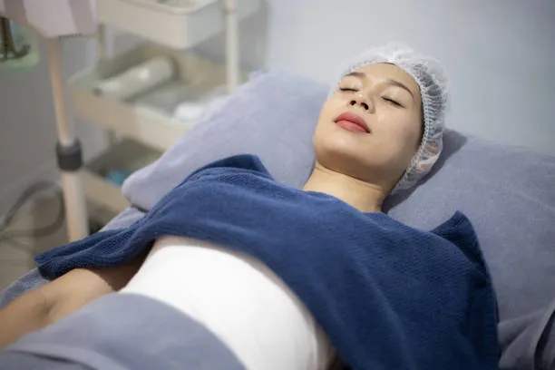 woman in hospital bed with surgical cap and chest bandages showing the first hours of recovery after post op breast lift surgery