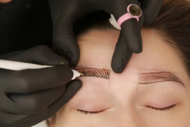 Professional carefully working on a patient’s eyebrows during the Microblading treatment process.