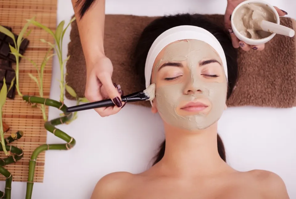 Over-head view of a woman receiving a green clay mask as part of her facial treatments.