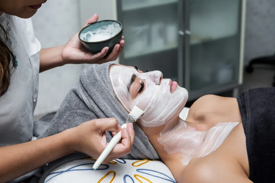 Close-up of an esthetician applying white foam on a client during facial treatments.