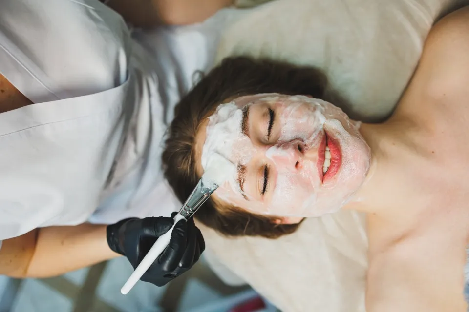 An esthetician in black gloves applies a foam product during facial treatments