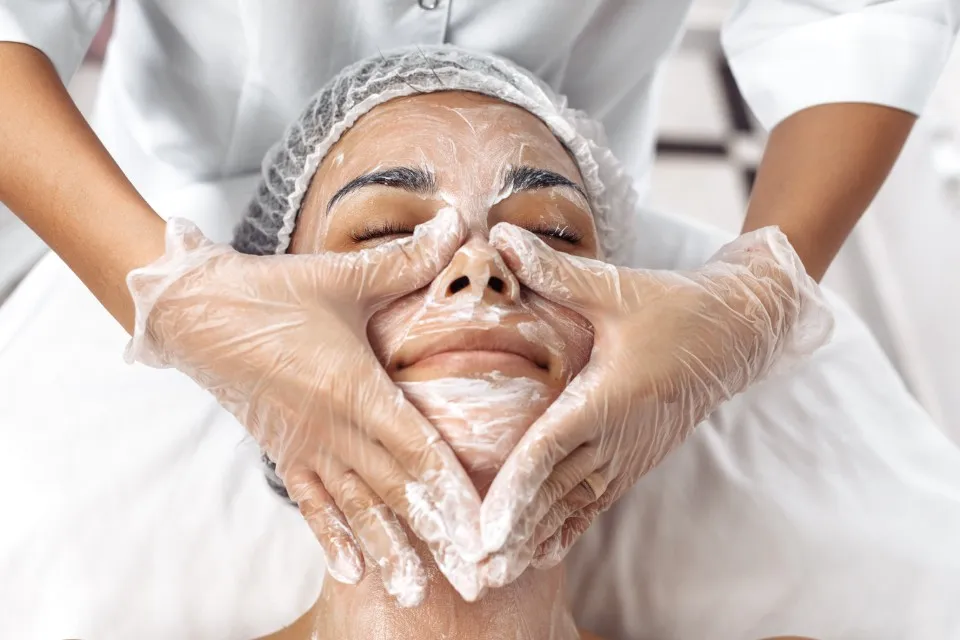 An esthetician wears gloves to massage a client’s face after applying facial treatments.