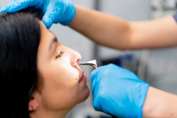Doctor performing nasal inspection during rhinoplasty recovery procedure.