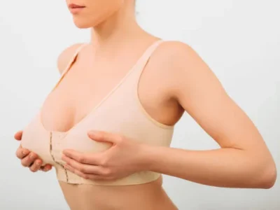 patient wearing post surgical bra and carefully adjusting breasts after post op breast lift